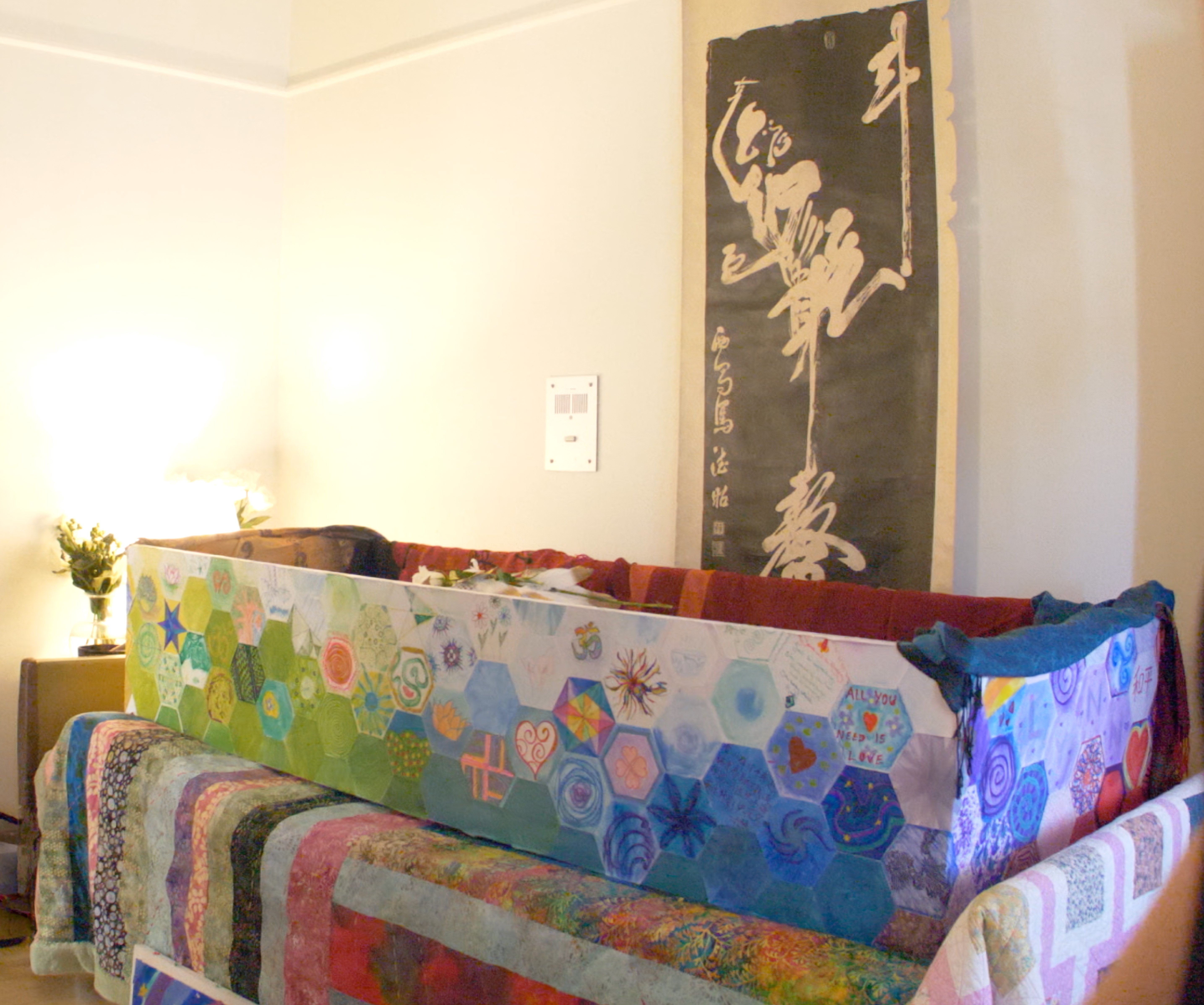 Lynn's coffin draped in a long mosaic of hand-painted hexagonal tiles in green, blue, and violet, beneath a tall Chinese calligraphy scroll.